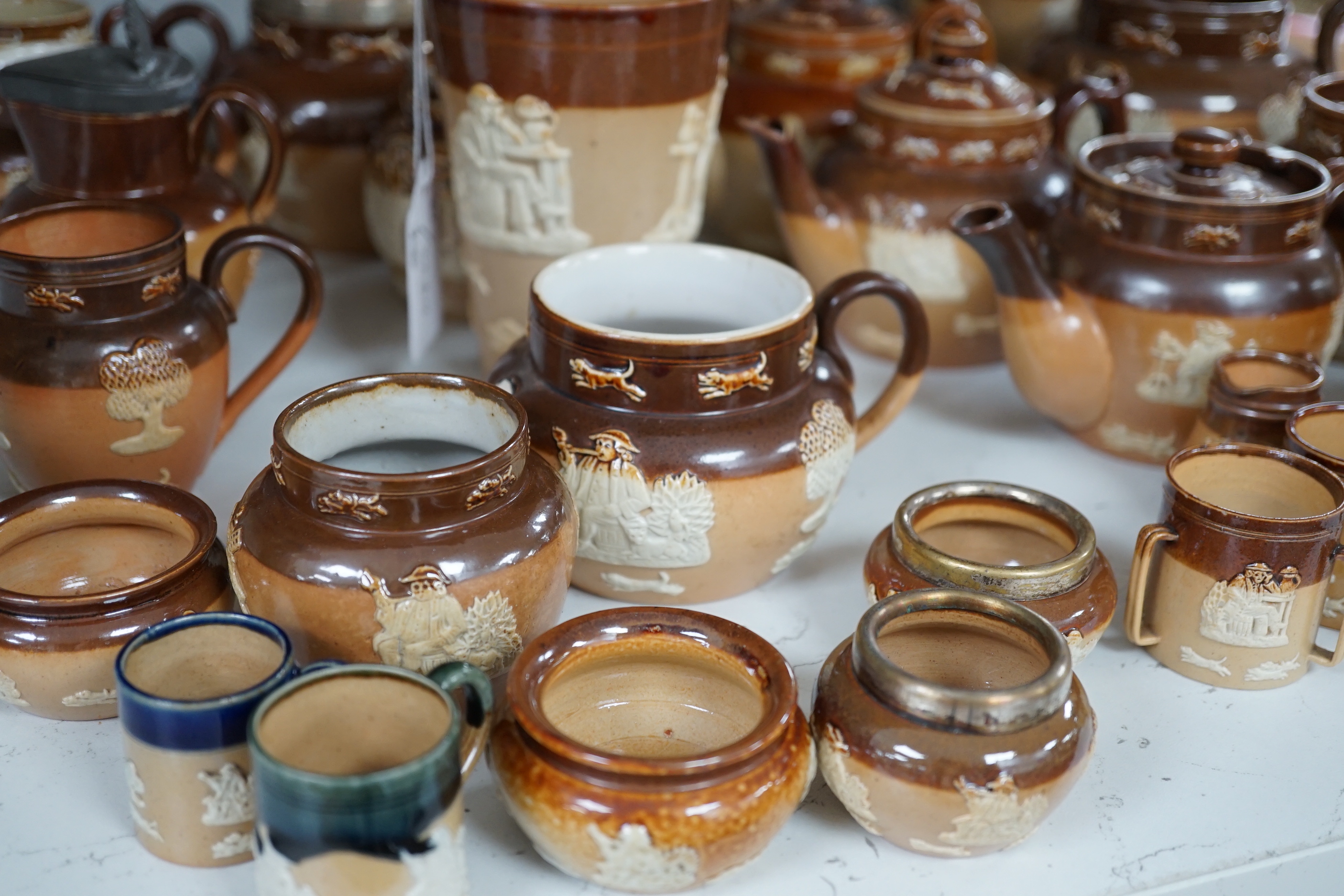 An assortment of Doulton stoneware including teapots, miniature tygs and twin handled pots, some silver mounted, largest 22cm wide